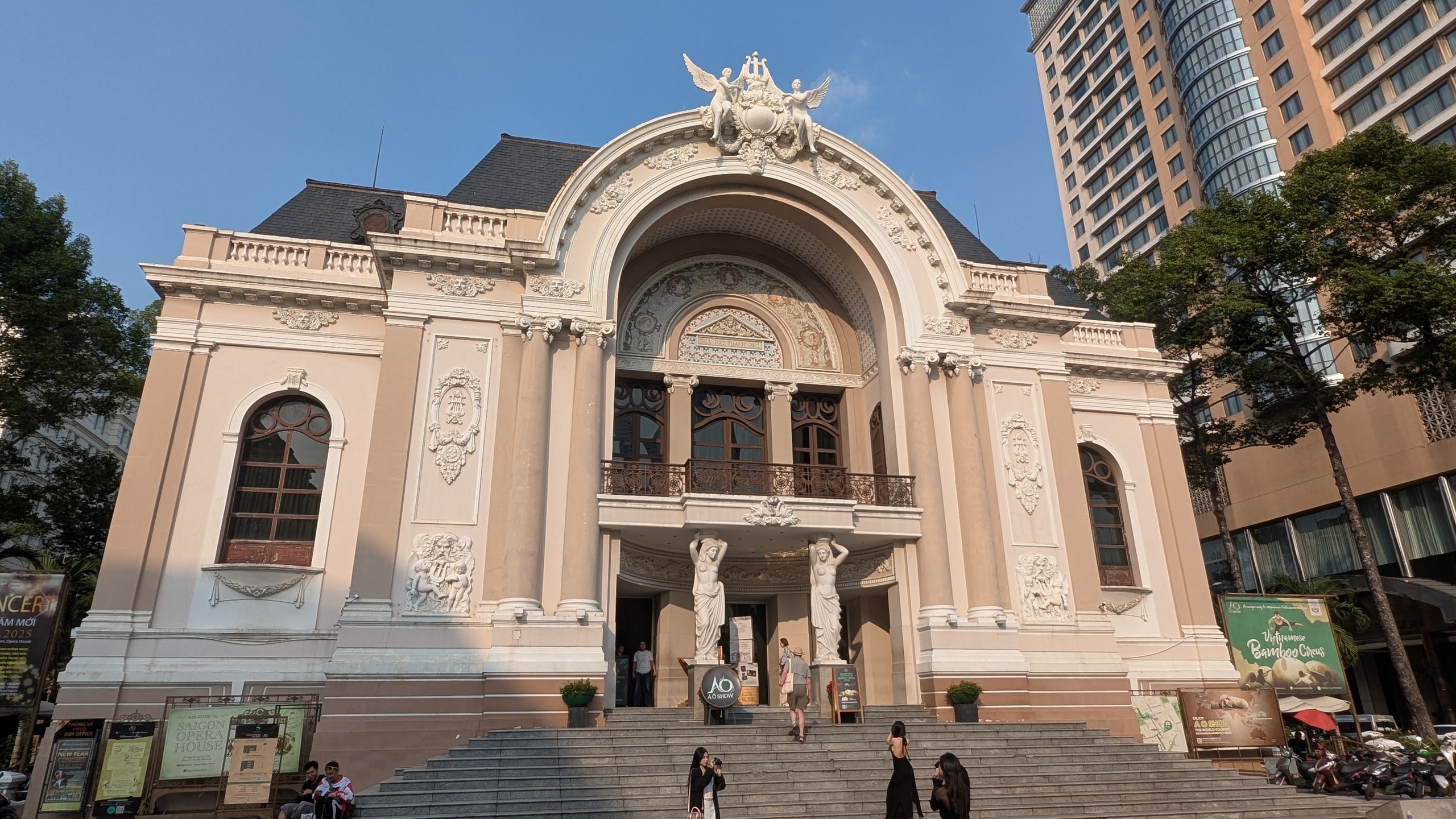 The pink Saigon Opera House facade with sculpted figures over the arched entrance and a modern high-rise beside it