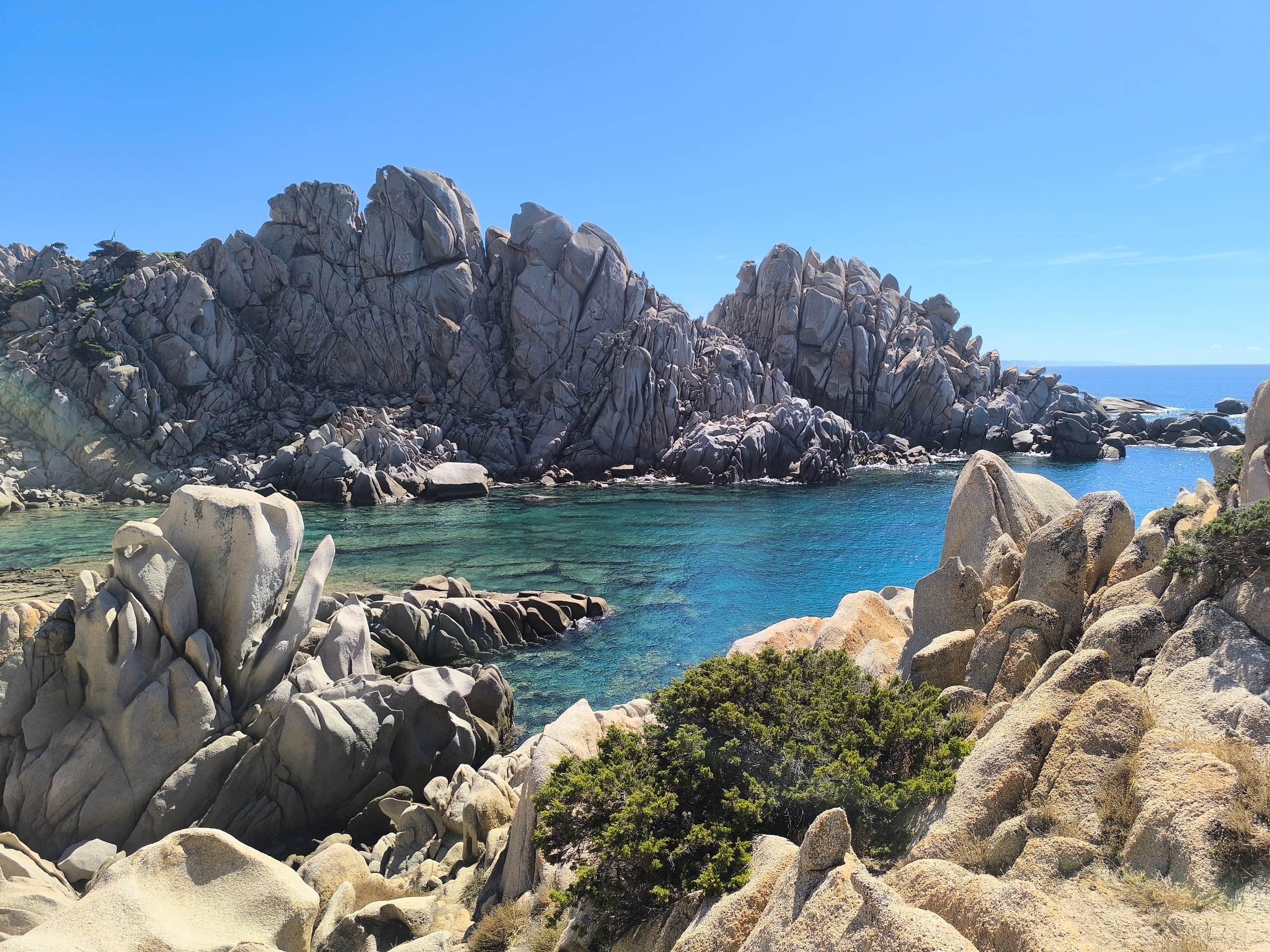 Tall weathered granite spires rising above a clear turquoise cove at Capo Testa in North Sardinia