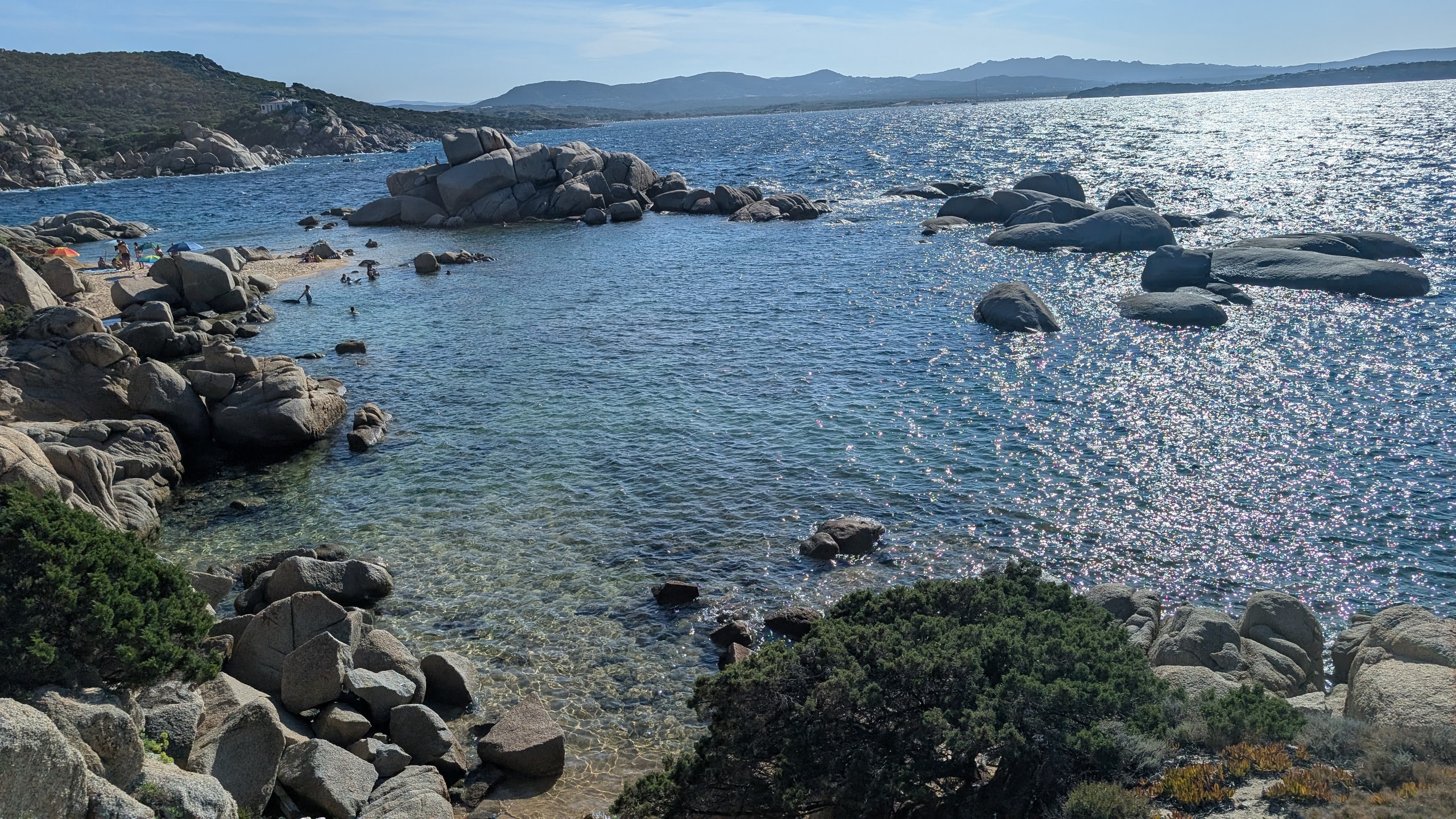 Weathered granite boulders and green maquis framing a turquoise cove on the Gallura coast of North Sardinia