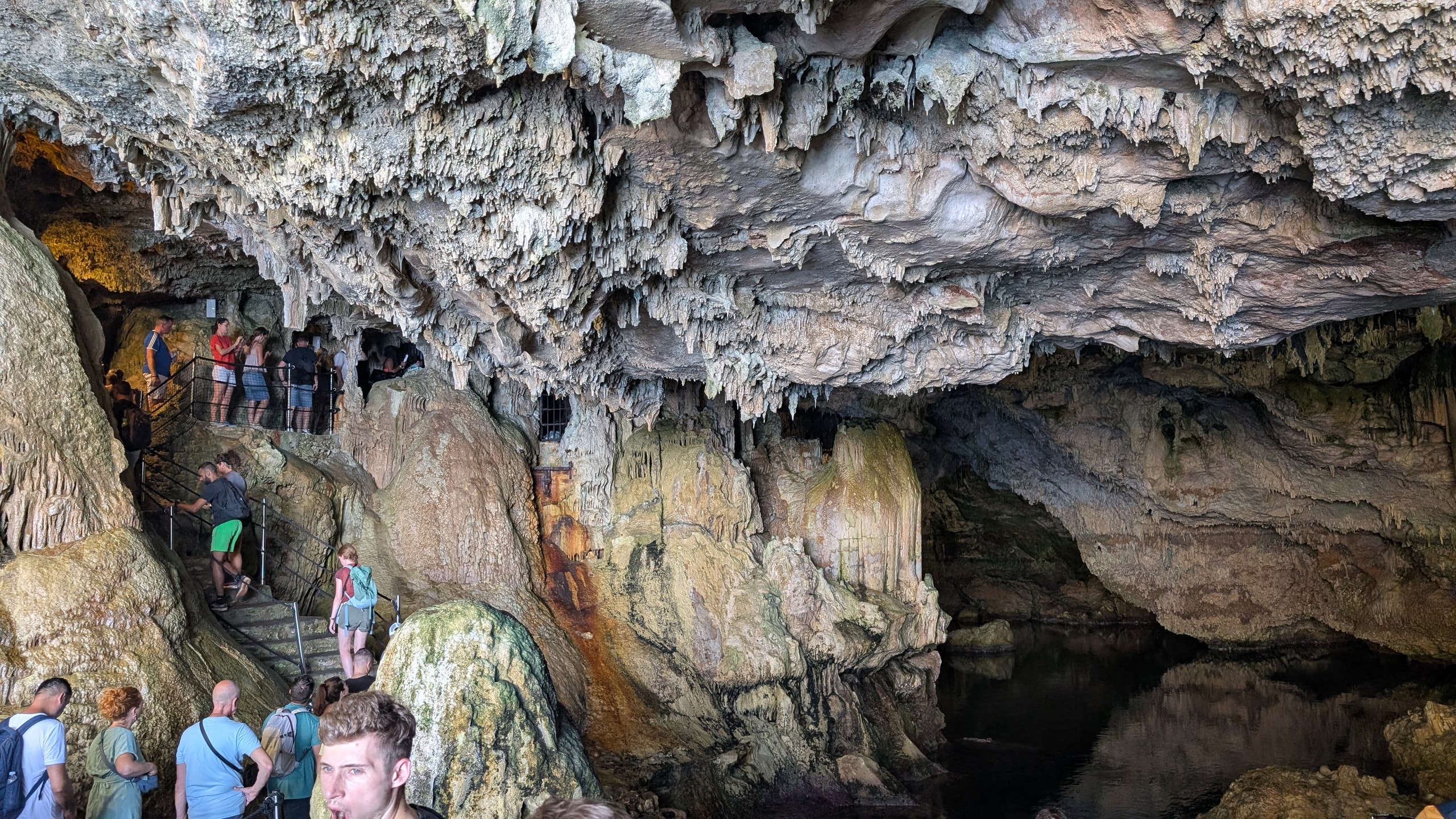 Visitors on a railed path inside Neptune’s Grotto among dense stalactites above an underground lake