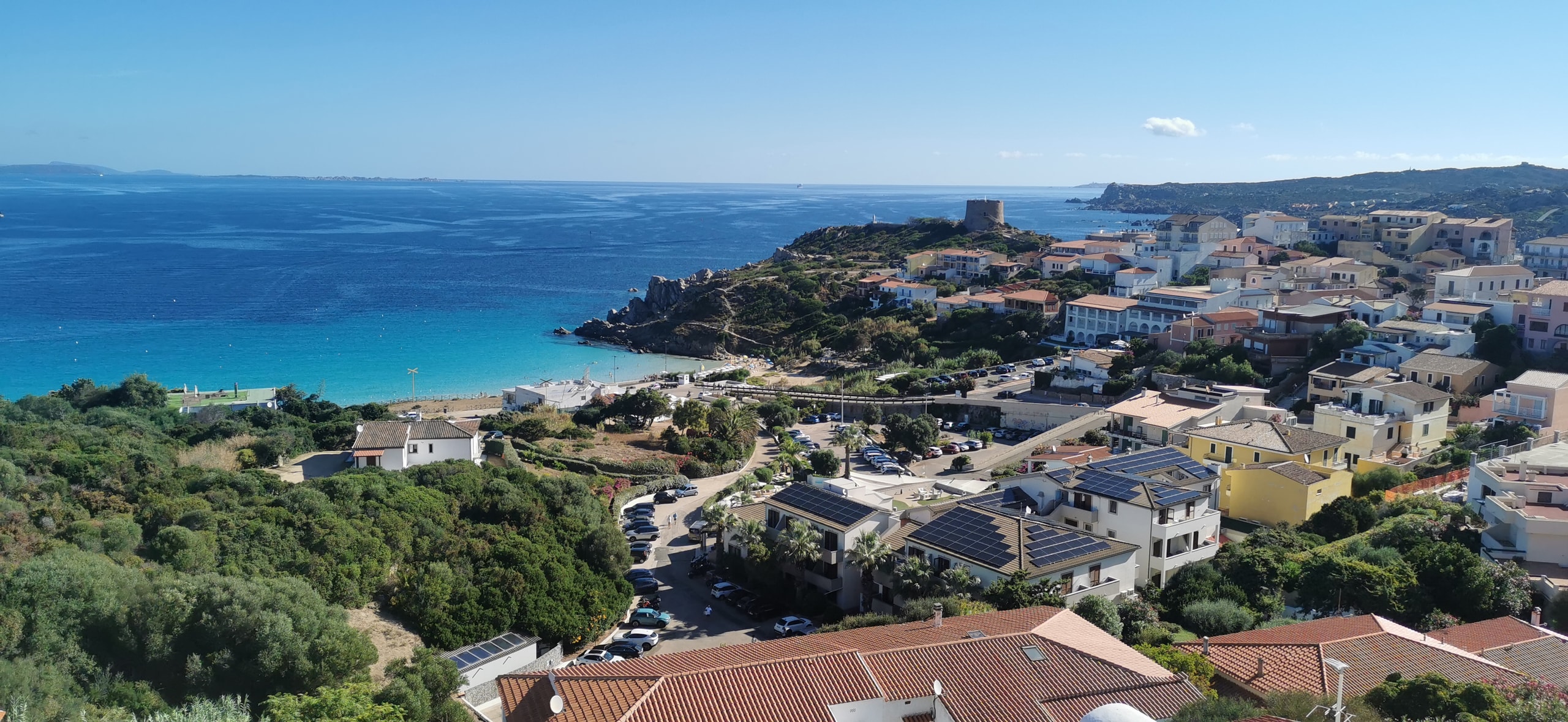 Santa Teresa Gallura spread across a hillside above a turquoise bay, with a stone watchtower on the rocky headland