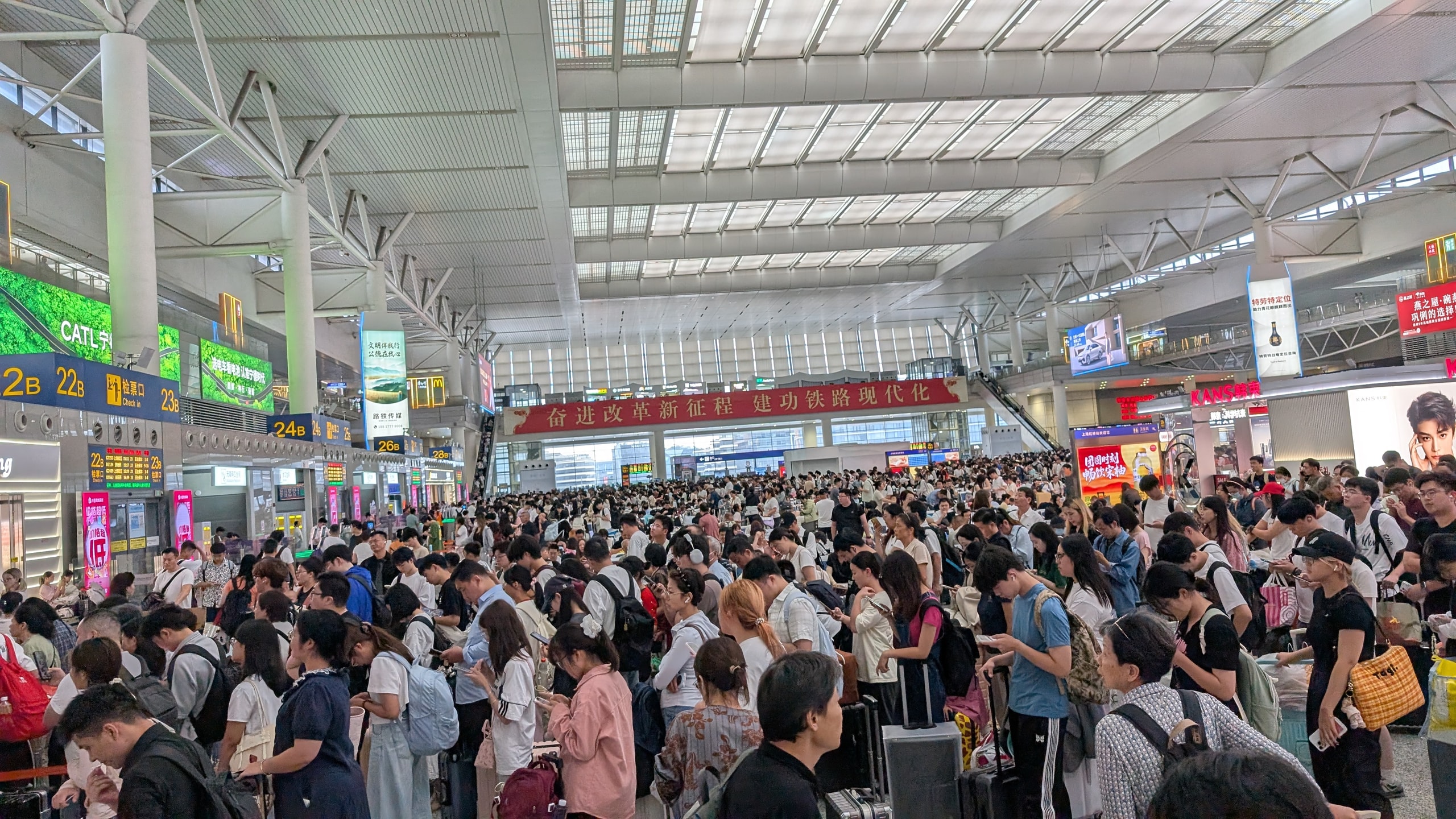 A vast railway station concourse packed shoulder to shoulder with thousands of travellers and suitcases under departure boards