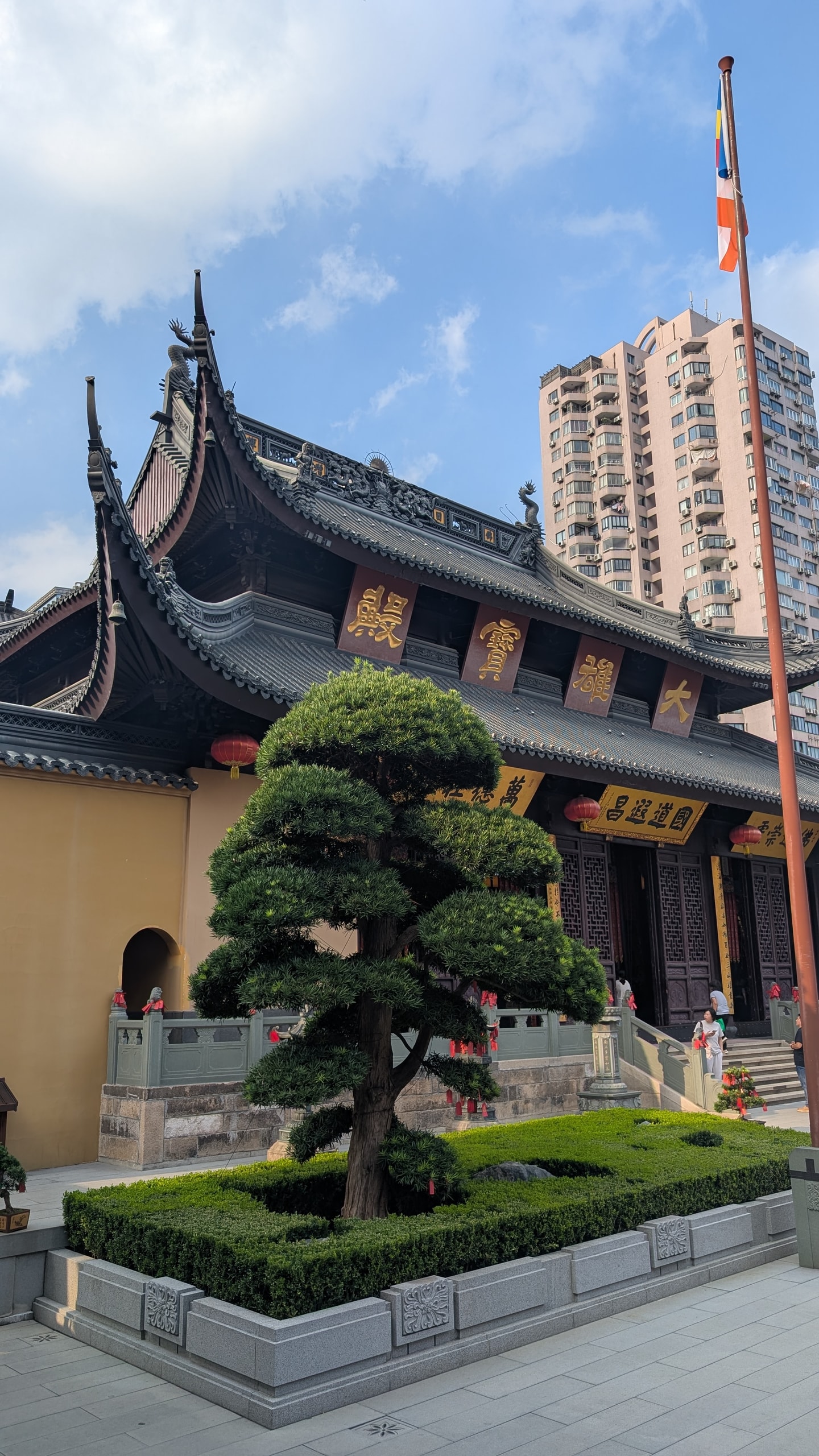 The tiled roof and gold plaque of the Jade Buddha Temple's main hall, with a tall pink apartment block rising directly behind it