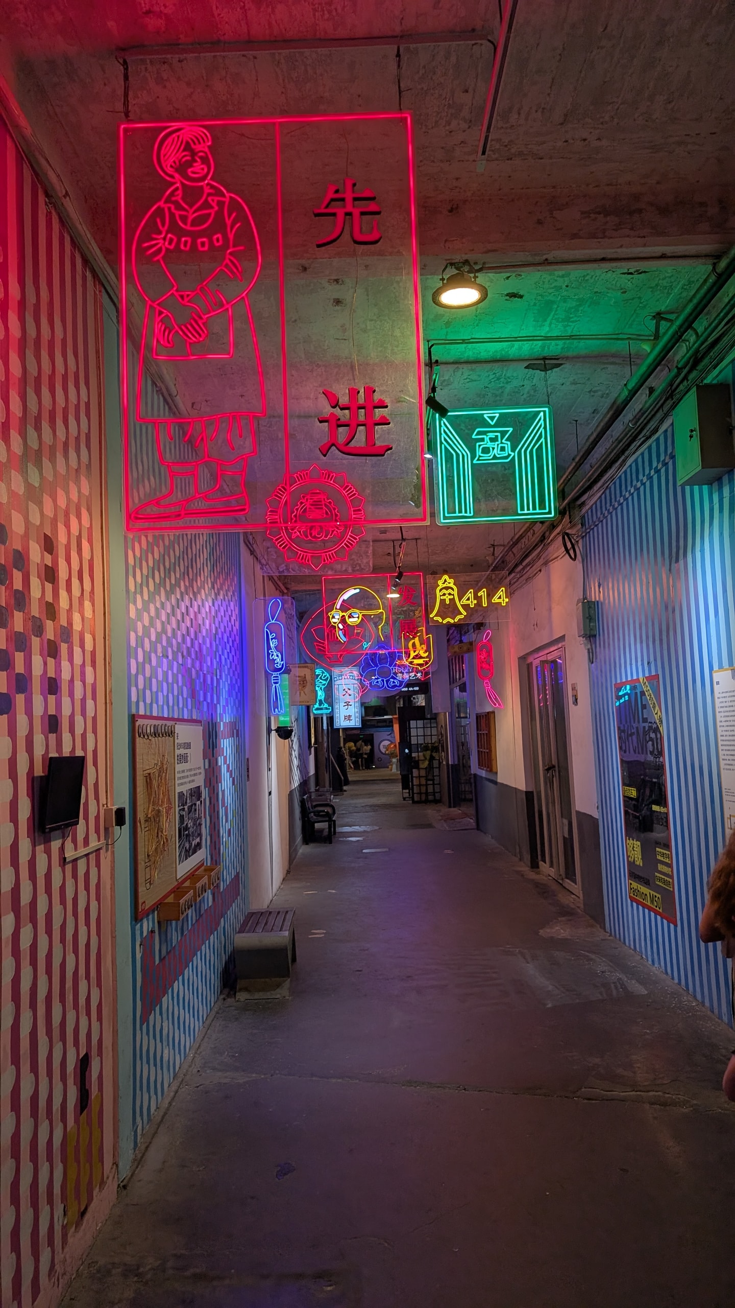 A narrow passage inside the M50 art district lit by pink and green neon signs hanging from a concrete ceiling