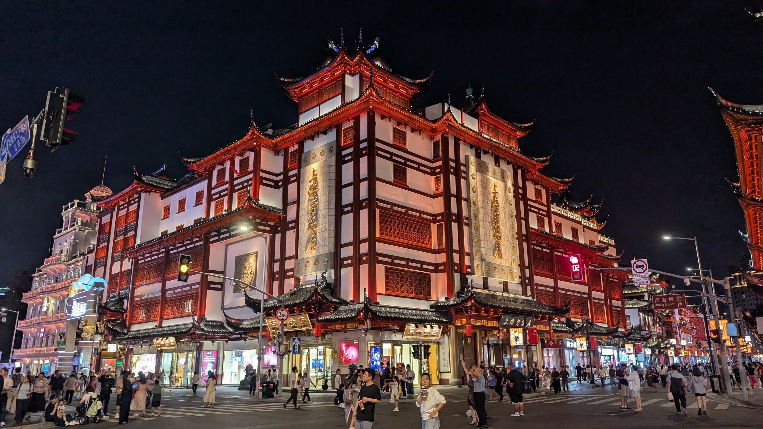 The Yu Garden bazaar at night, its multi-tiered temple-style buildings lit gold and red above a crowded street corner