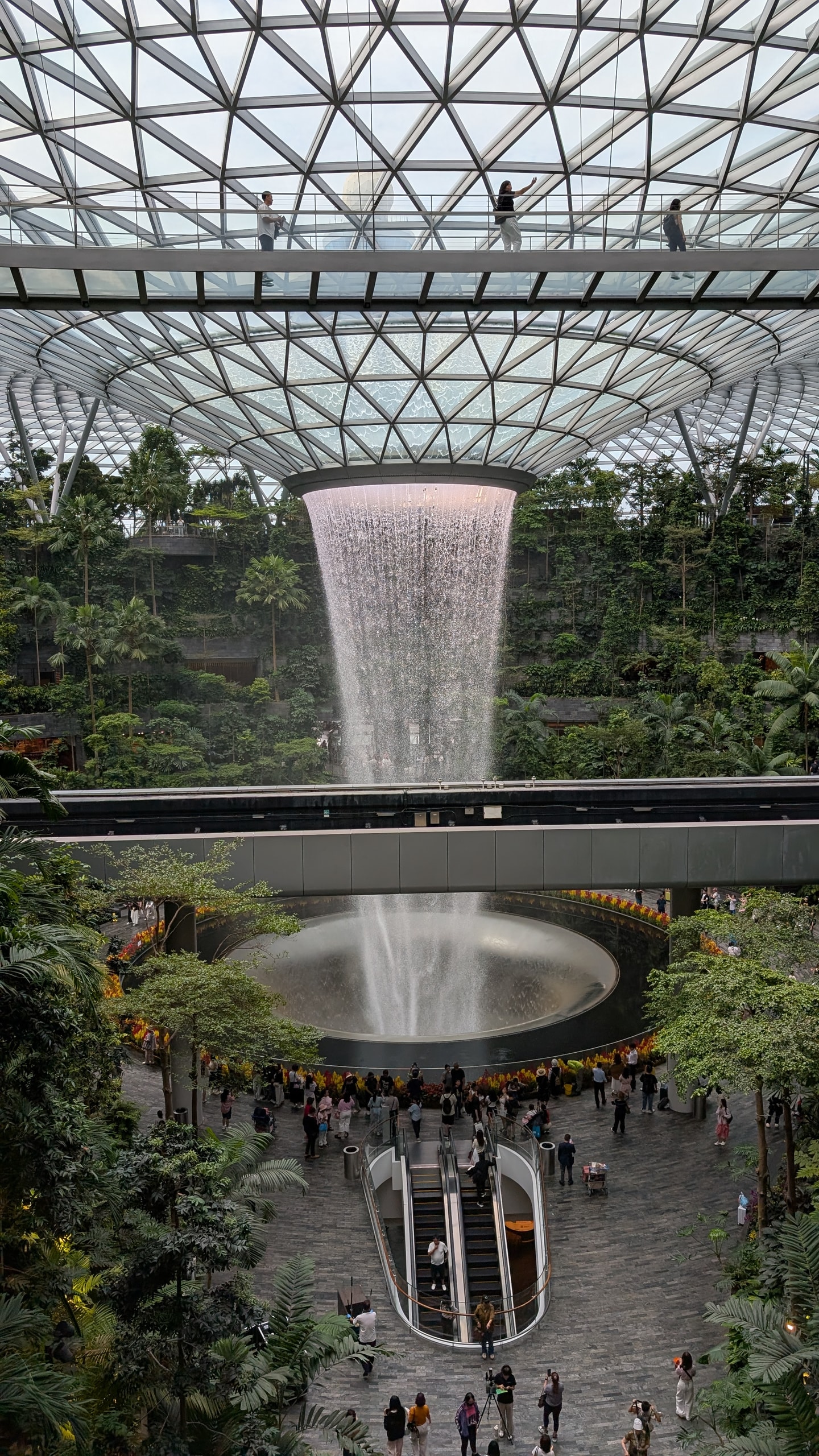 The Rain Vortex waterfall falling through the glass roof of Jewel Changi Airport into a ring of terraced forest