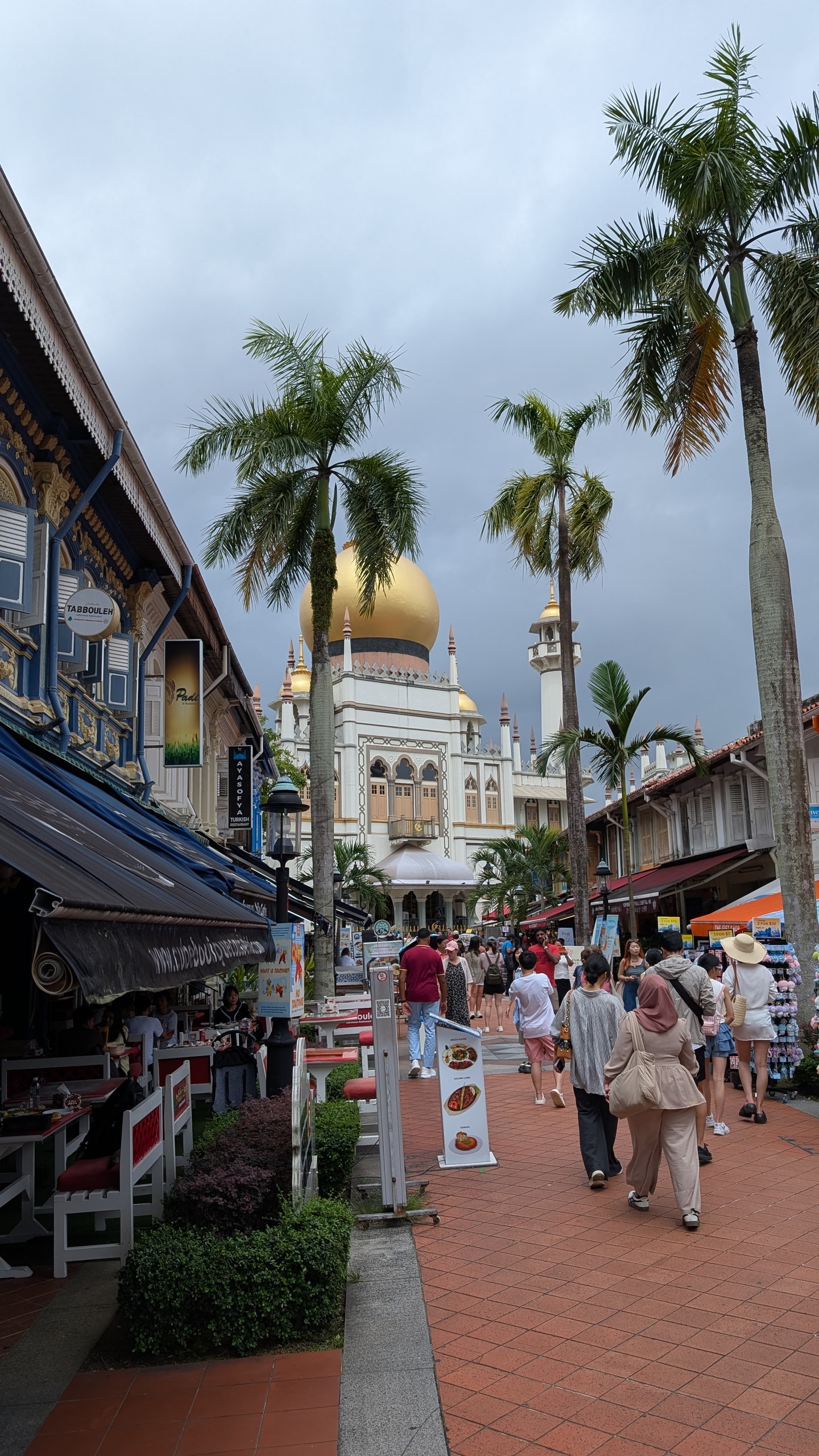 Bussorah Street in Kampong Glam lined with palms and shophouse restaurants, leading to the golden dome of Sultan Mosque