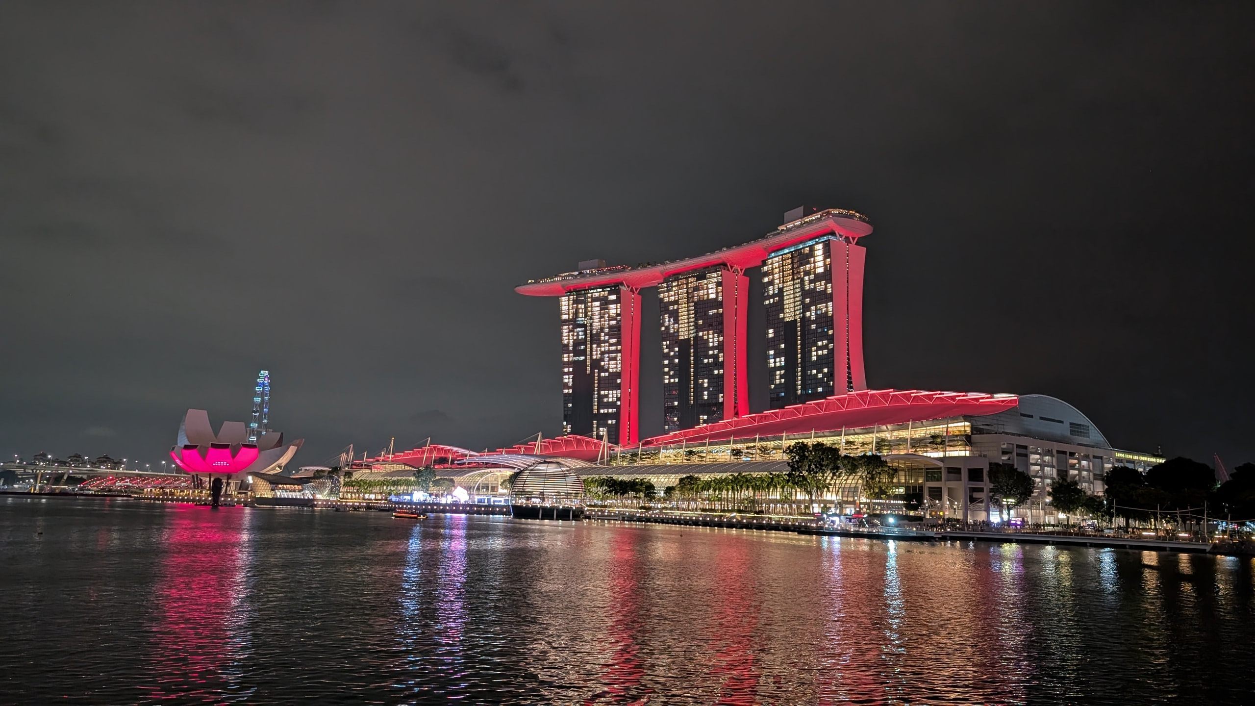 Marina Bay Sands floodlit red at night above the water, with the pink lotus shape of the ArtScience Museum on the left