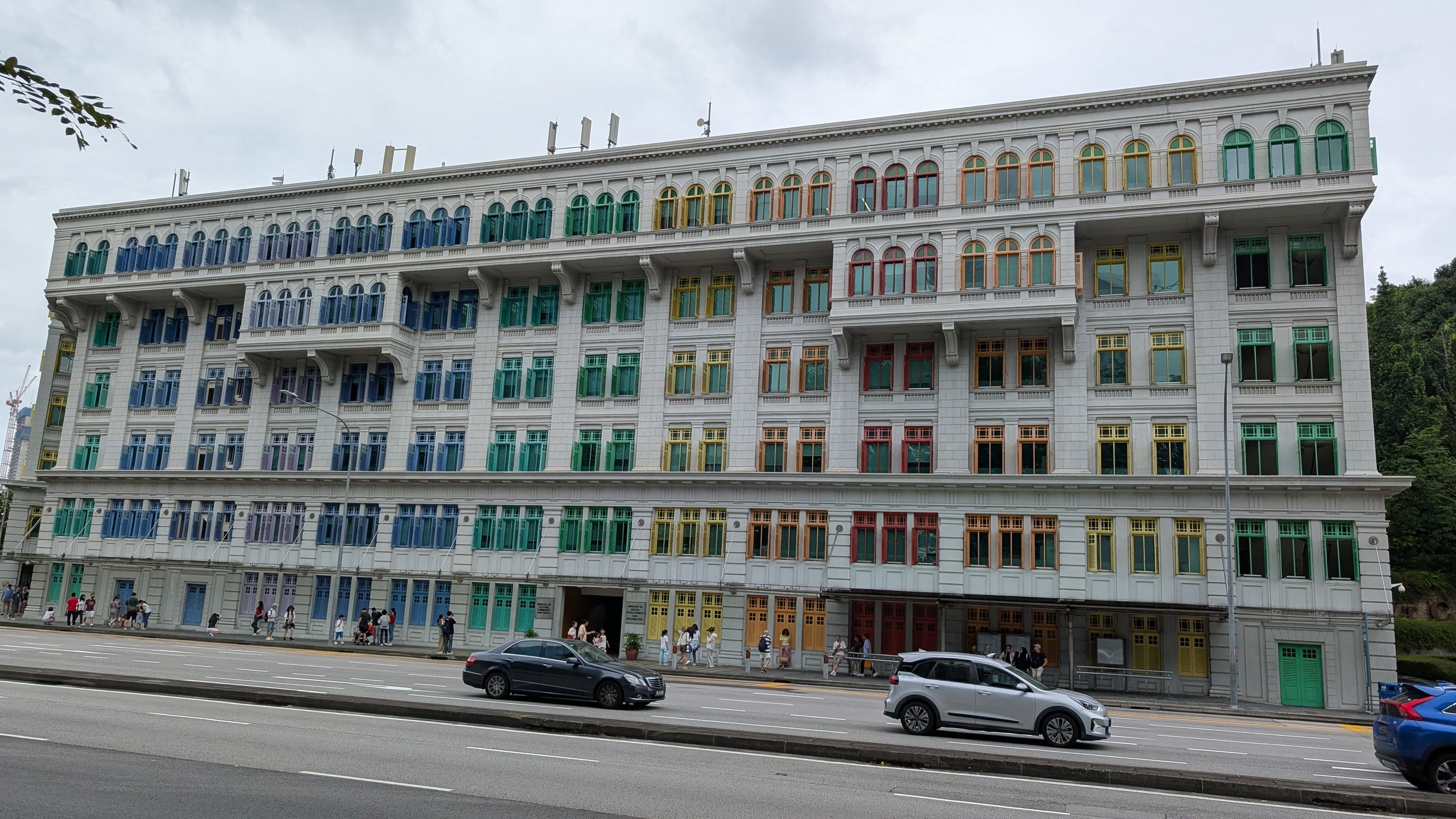 The Old Hill Street Police Station, a white colonial building with 927 window shutters painted in rainbow colours, seen from across the road