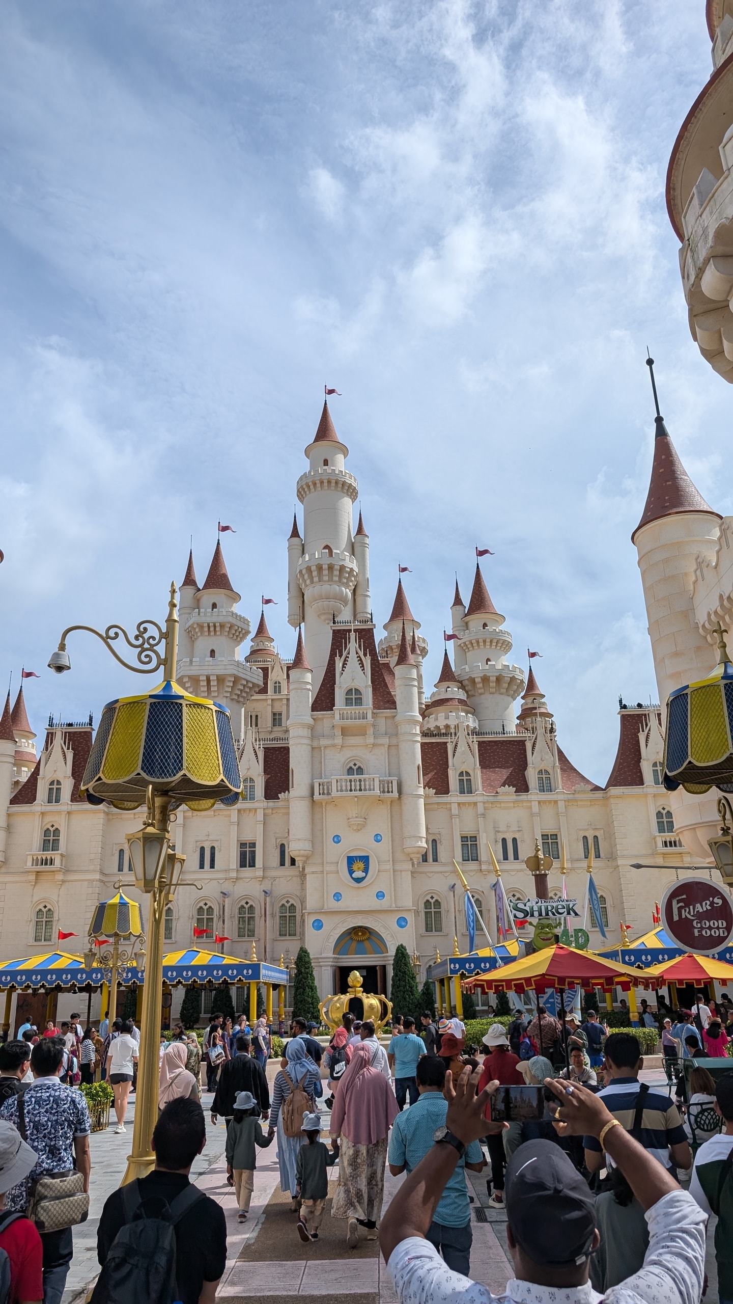 A crowd holding phones up in front of the Far Far Away castle at Universal Studios Singapore under a blue sky