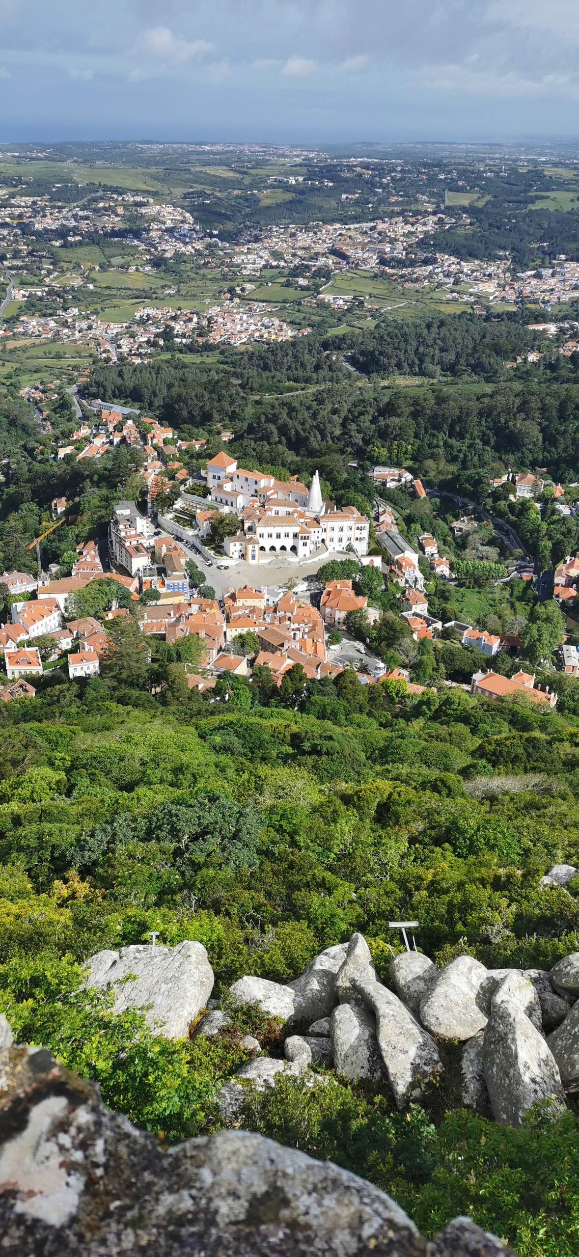 Looking down from granite boulders on the Moorish Castle toward Sintra town, with the National Palace’s twin white chimneys in the valley