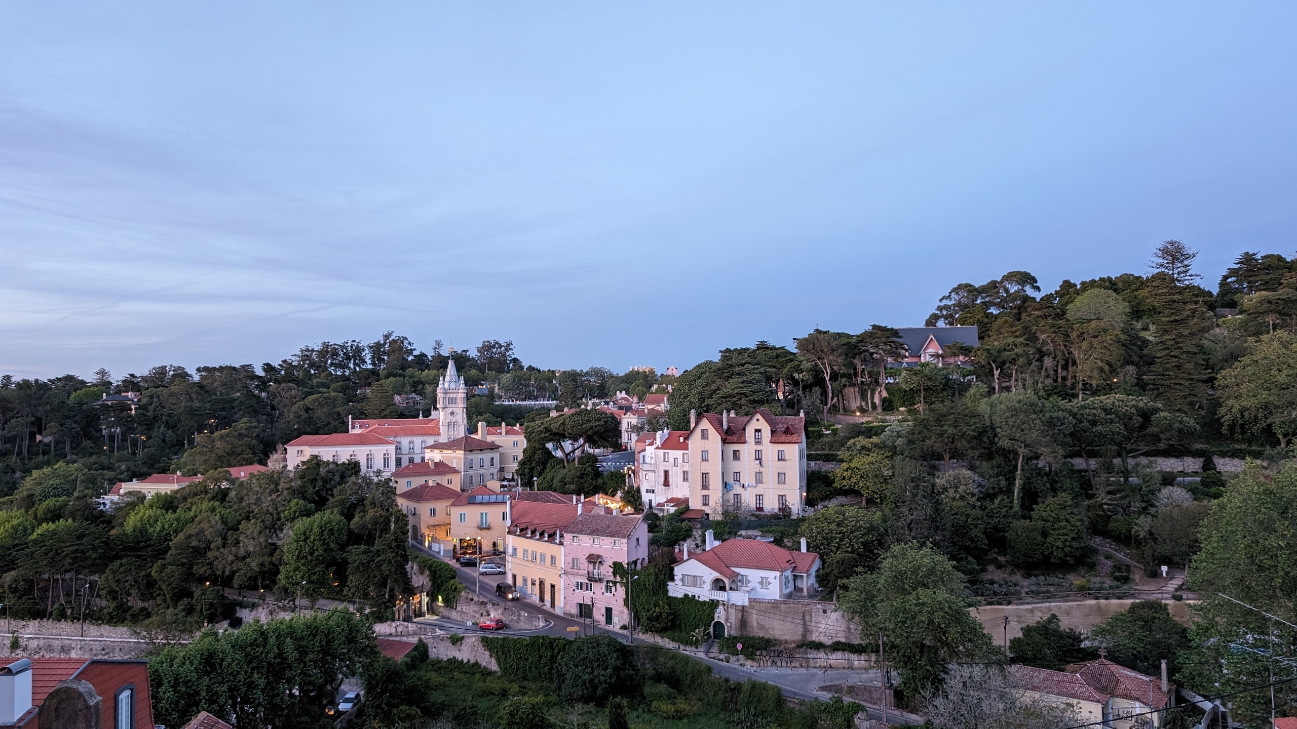 Terracotta rooftops and a white church tower in Sintra’s historic centre at dusk, with forested hills behind the houses