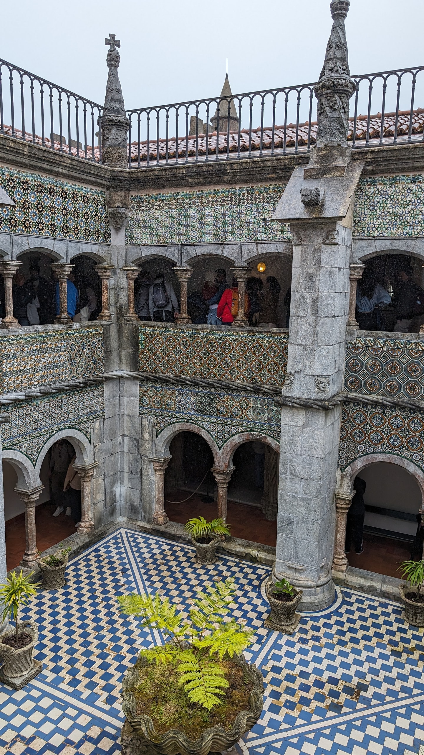 Looking down into Pena Palace’s tiled cloister, with arched galleries, azulejo walls, and a zigzag floor around stone planters