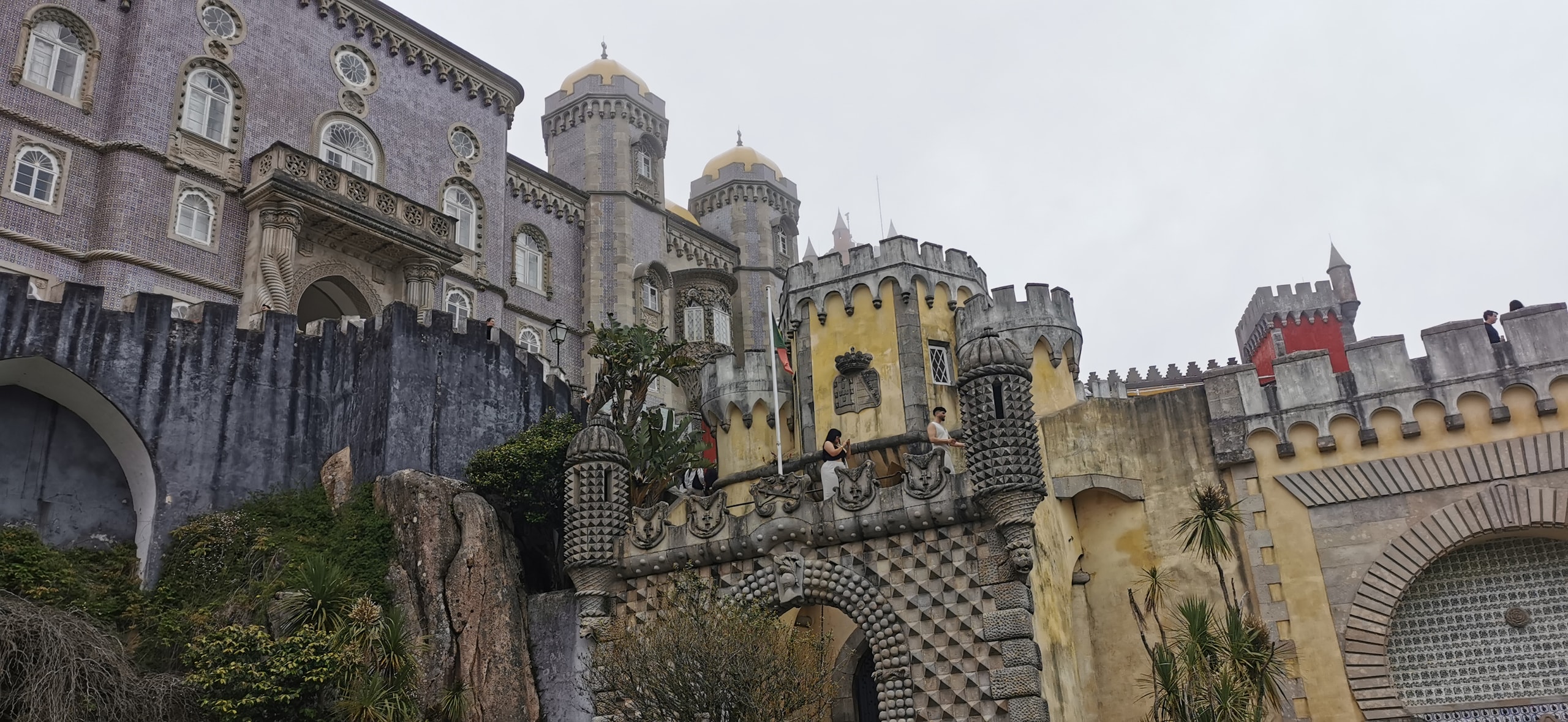 Yellow walls, lavender tiles, onion domes and a red tower of Pena Palace in Sintra against an overcast sky