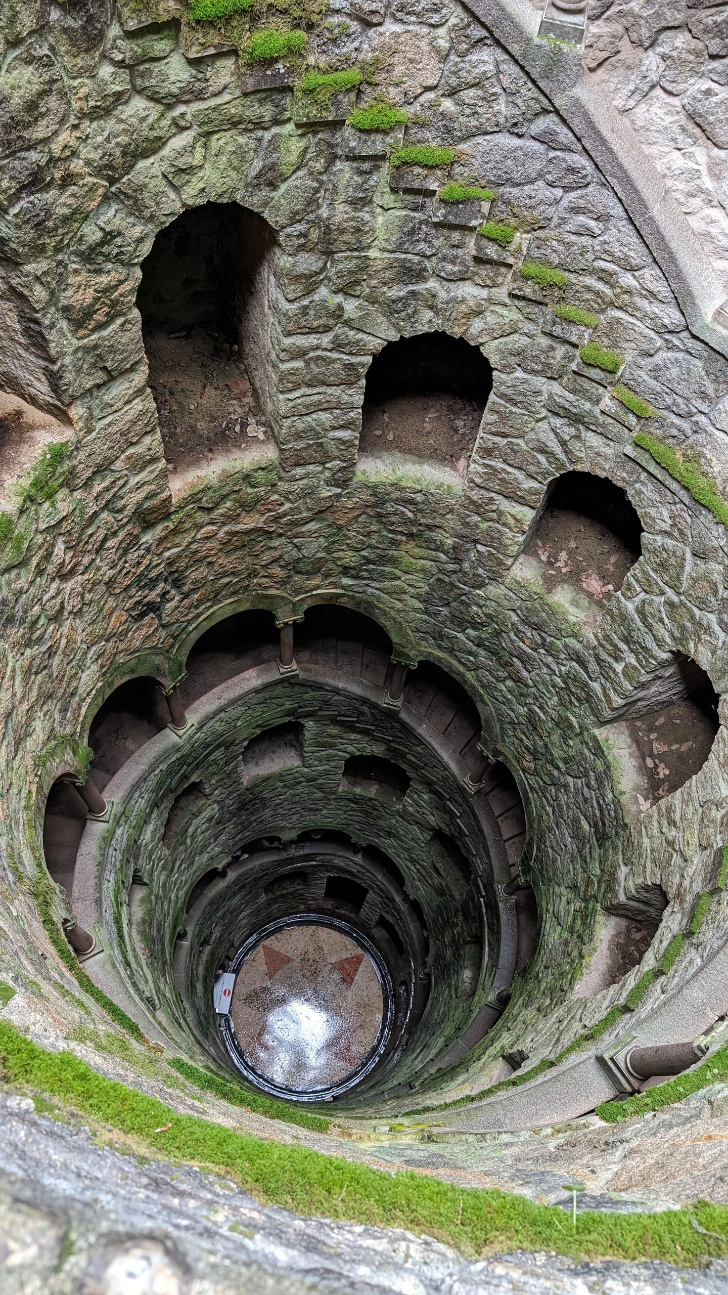 Looking down the spiral stone staircase of the Initiation Well at Quinta da Regaleira toward the mosaic floor at the bottom