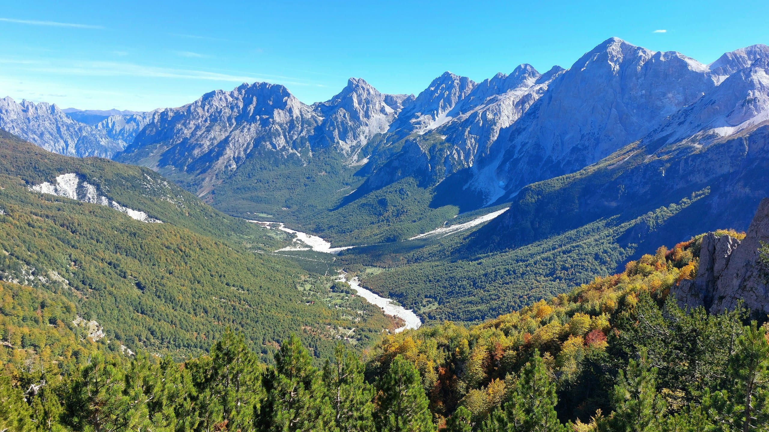 High view over a limestone mountain valley with autumn forests and a pale riverbed in the Albanian Alps near Theth and Valbona