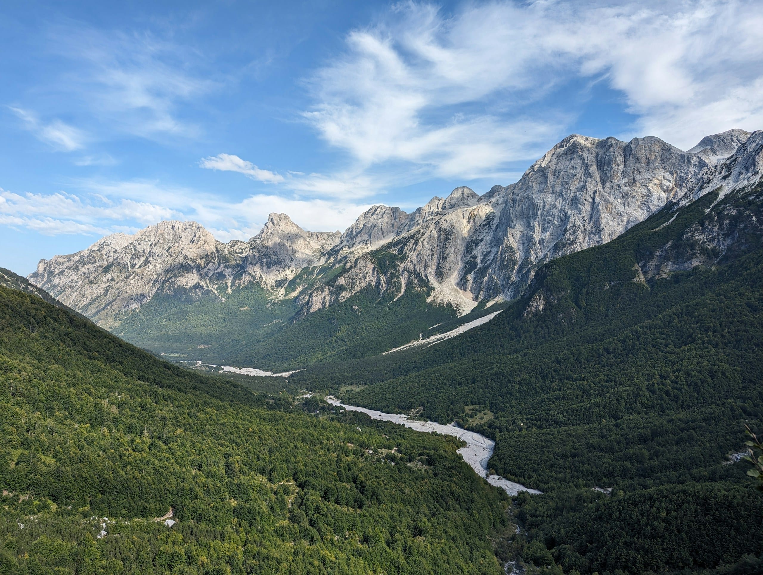 Pale river and gravel beds winding through the Valbona valley with steep Albanian Alps peaks on both sides