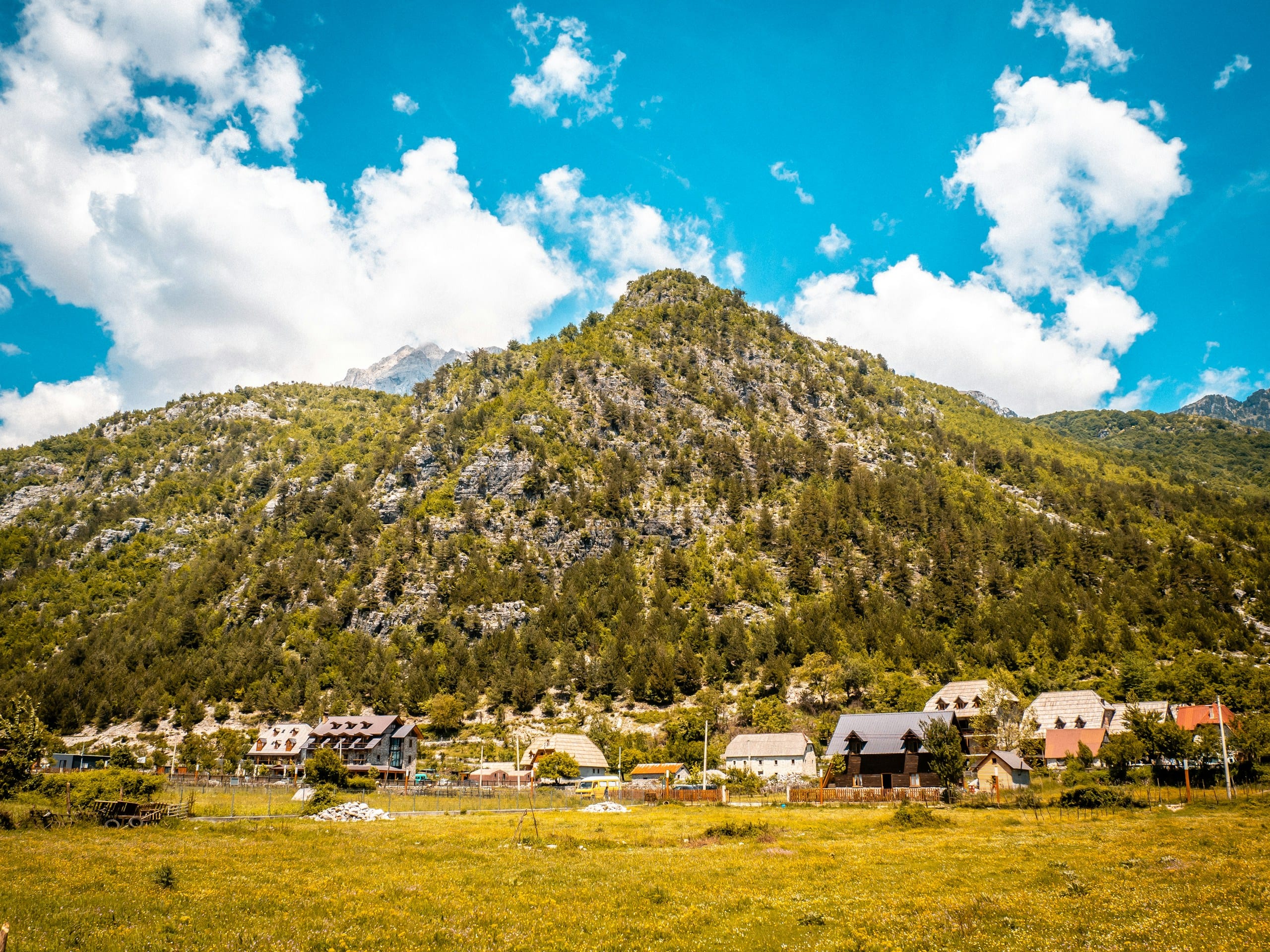 Stone houses of Theth village scattered across a green valley floor beneath steep Albanian Alps peaks
