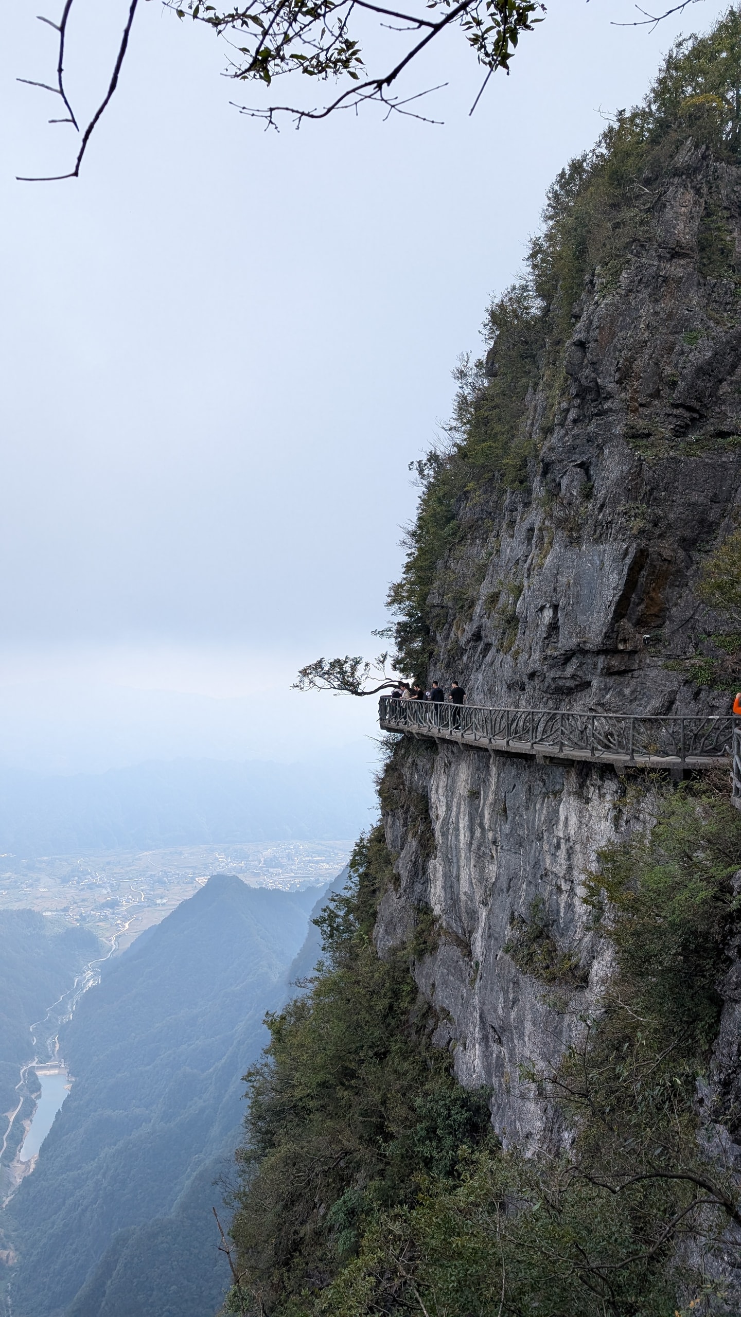 A narrow walkway clinging to a sheer limestone cliff on Tianmen Mountain with a hazy valley and city far below