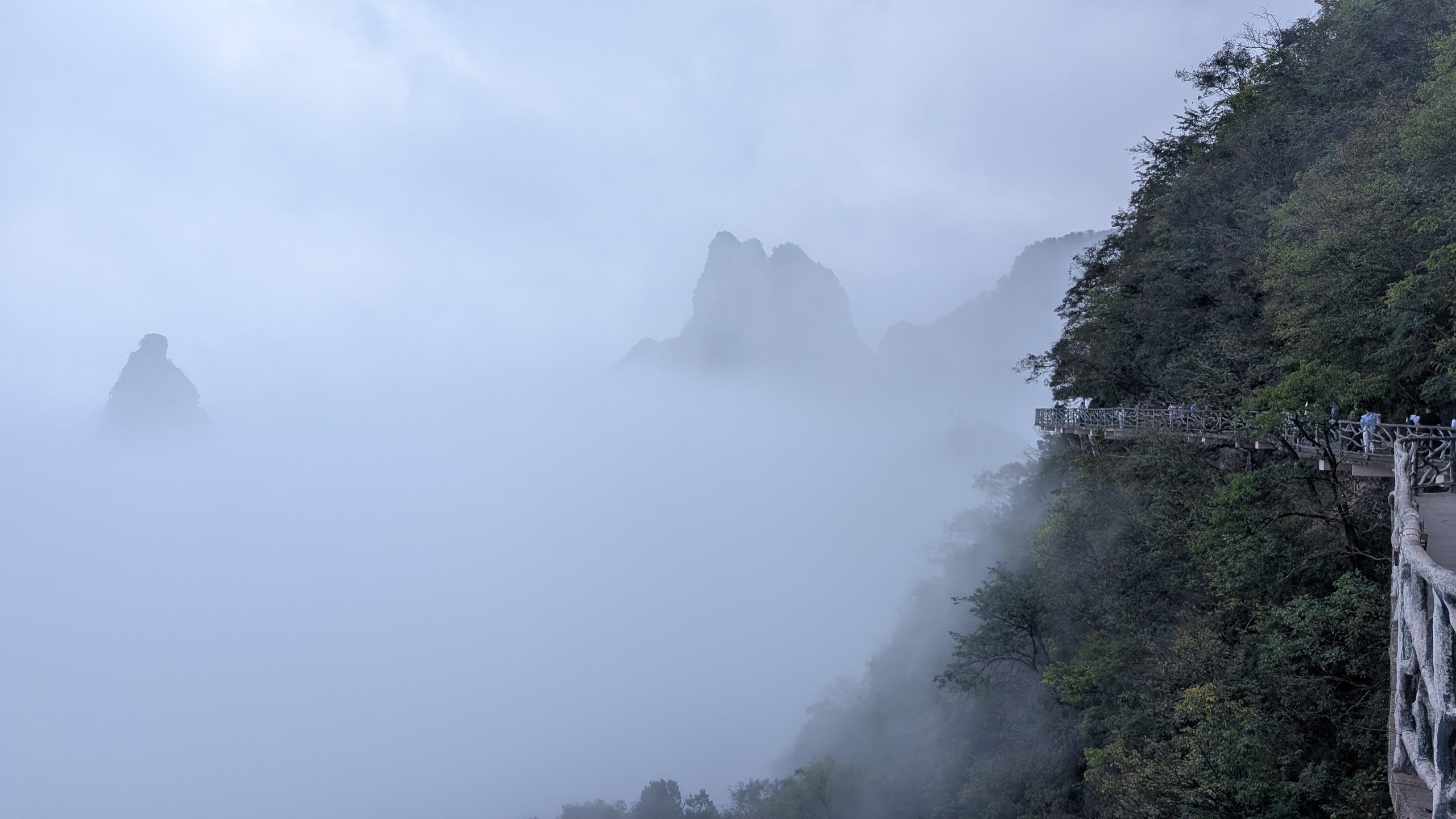 Rock towers rising out of thick fog beside a cliff walkway on Tianmen Mountain in Hunan, China