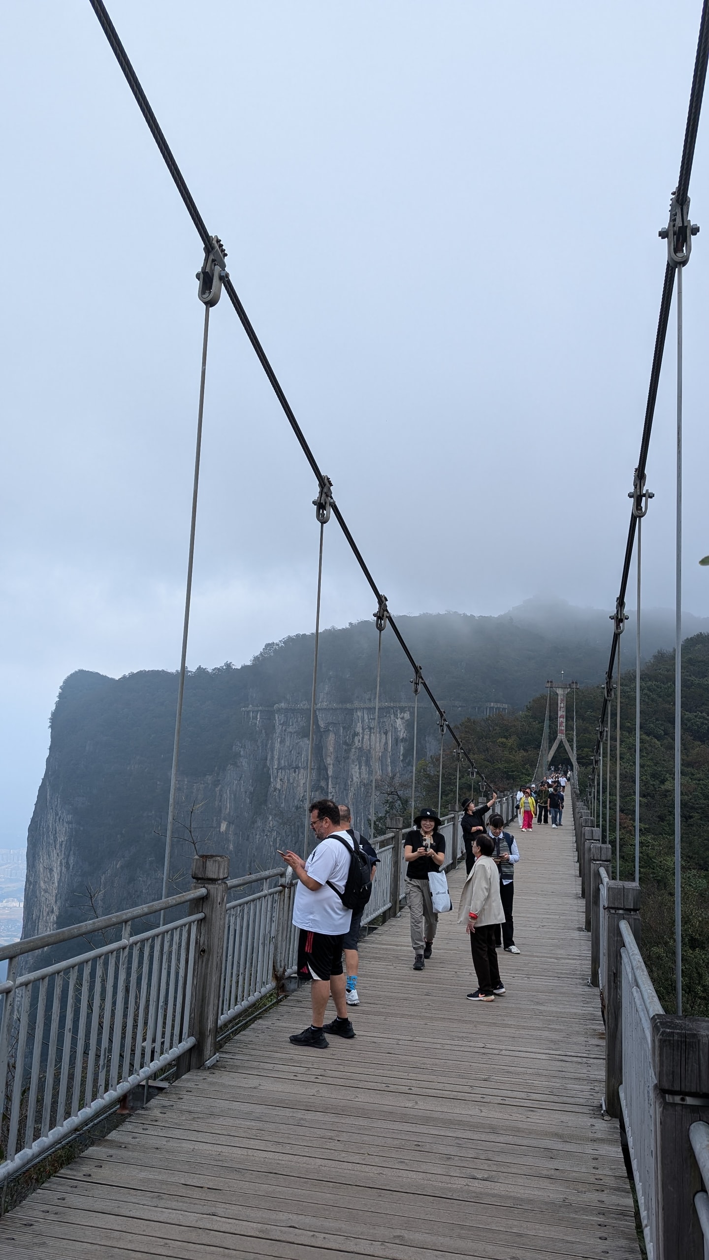 Visitors crossing a timber suspension bridge on the summit ridge of Tianmen Mountain with cloud sitting on the peaks behind