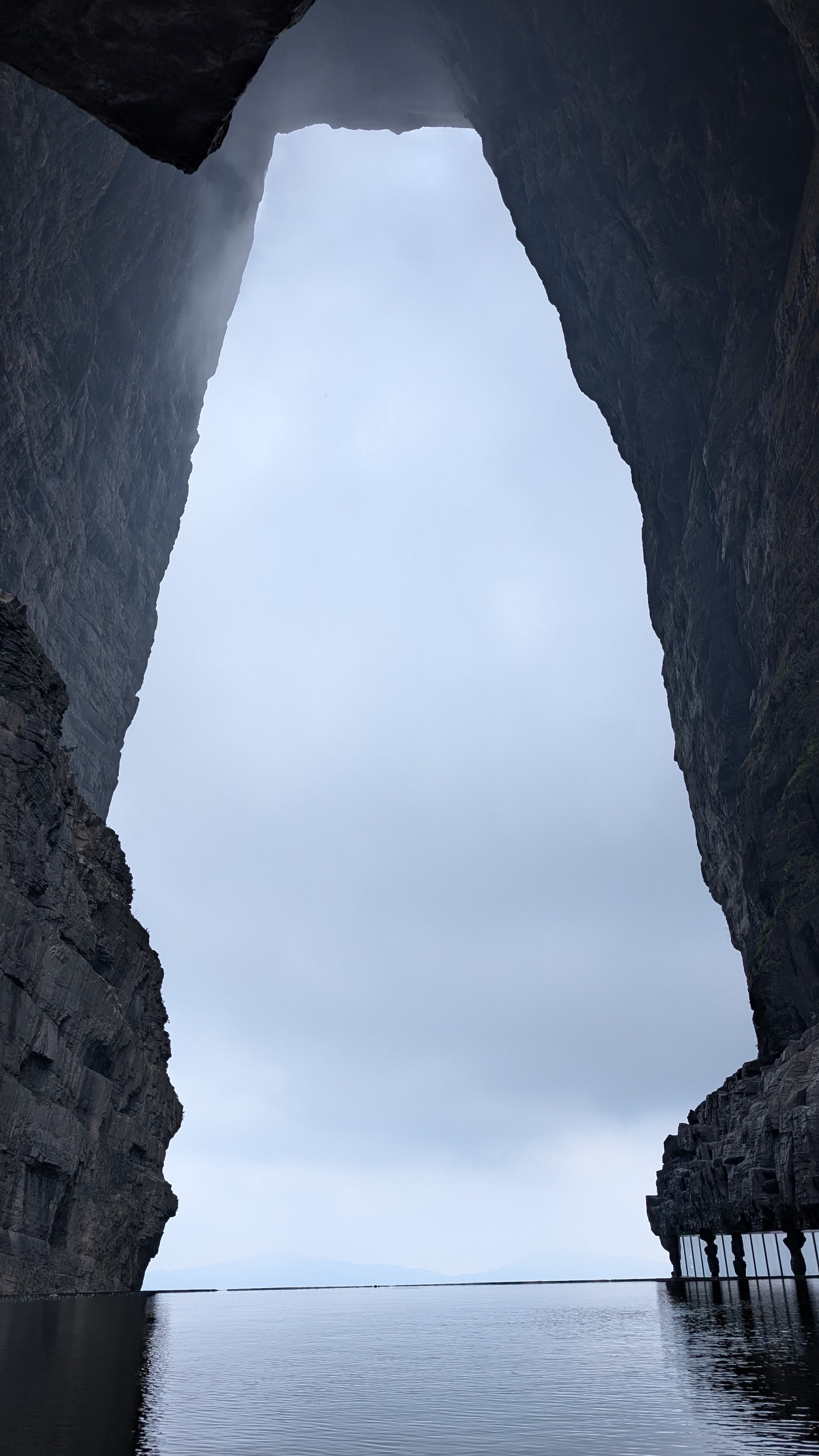 Looking up through the Tianmen Cave arch at pale sky framed by dark overhanging limestone walls