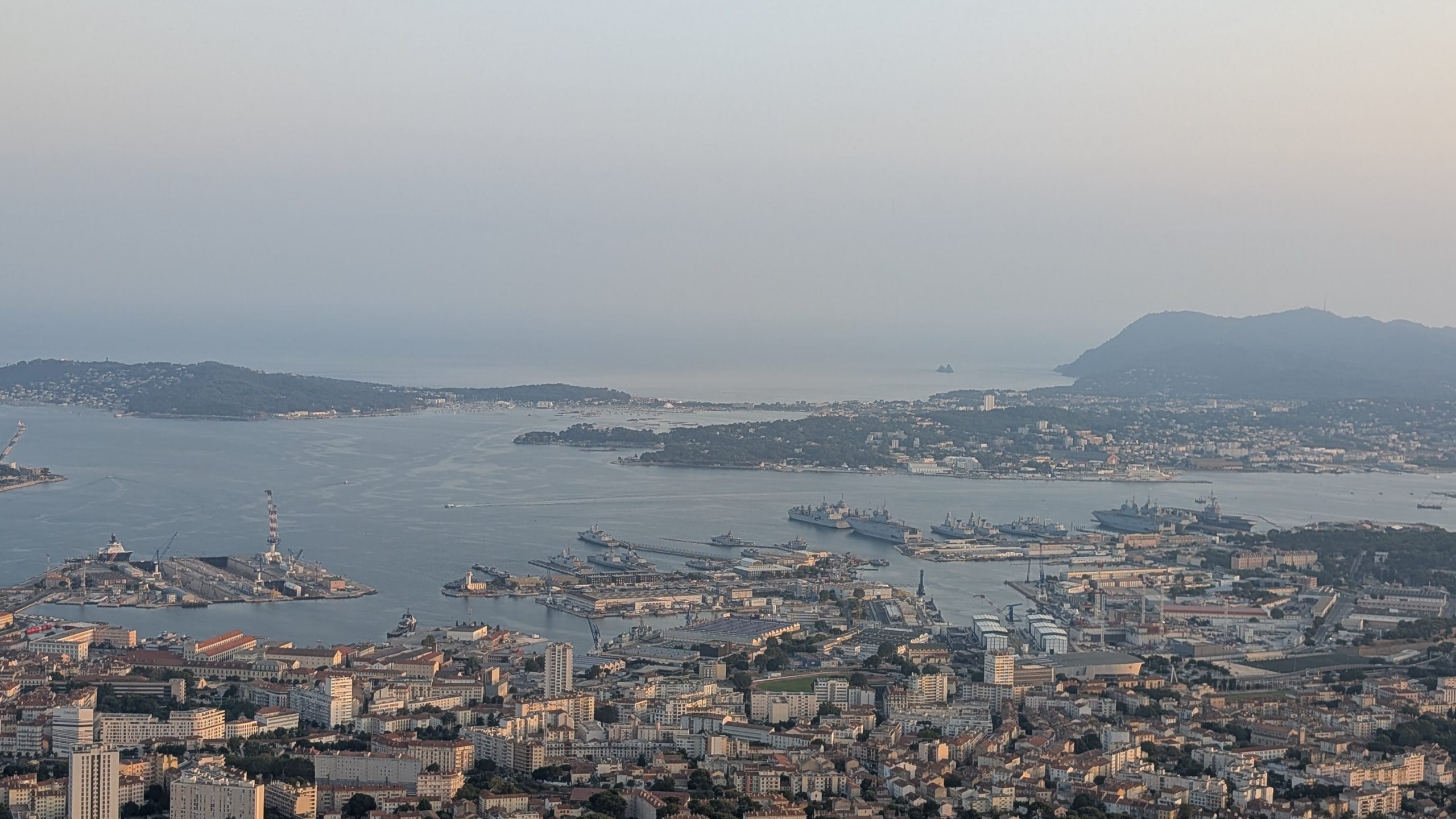 Warships moored along the naval arsenal quays in Toulon harbour, seen from Mont Faron with the Saint-Mandrier peninsula beyond