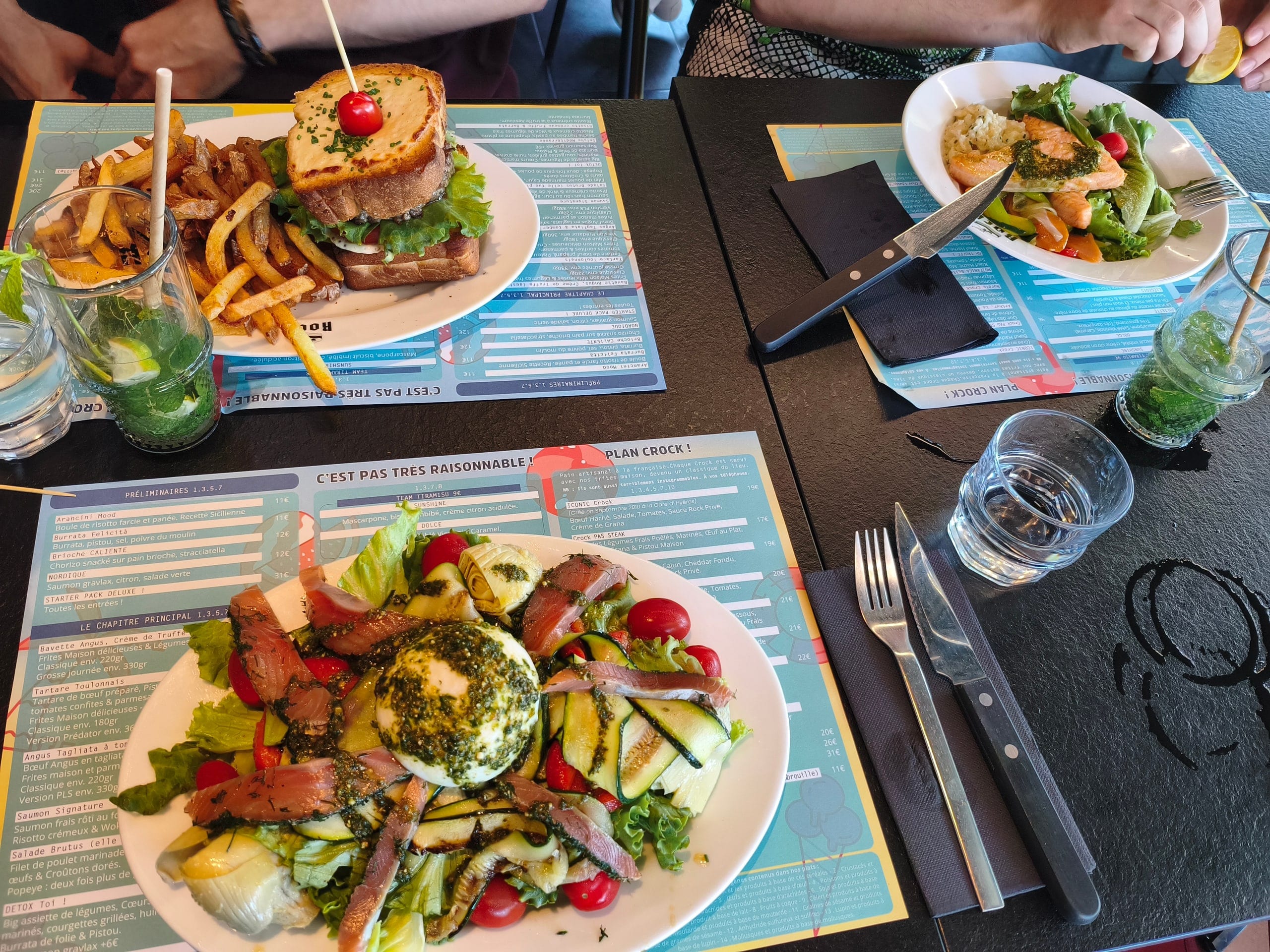 A burrata salad with grilled courgettes and cured fish, a croque-monsieur with hand-cut fries, and two mojitos on a restaurant table in Toulon