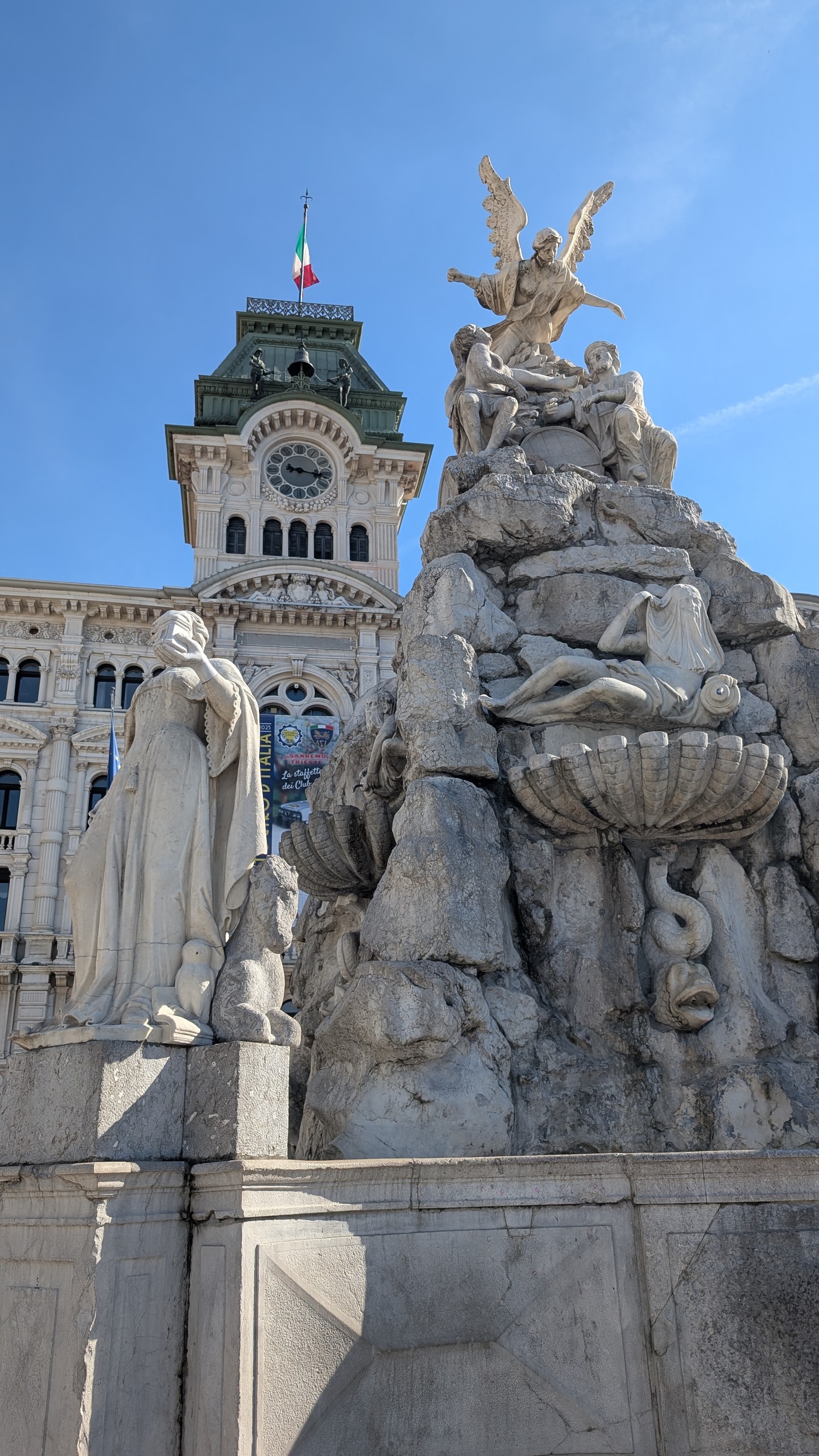 The Fountain of the Four Continents in Piazza Unità d'Italia, topped by a winged figure, with the town hall clock tower and its two bronze bell-strikers behind