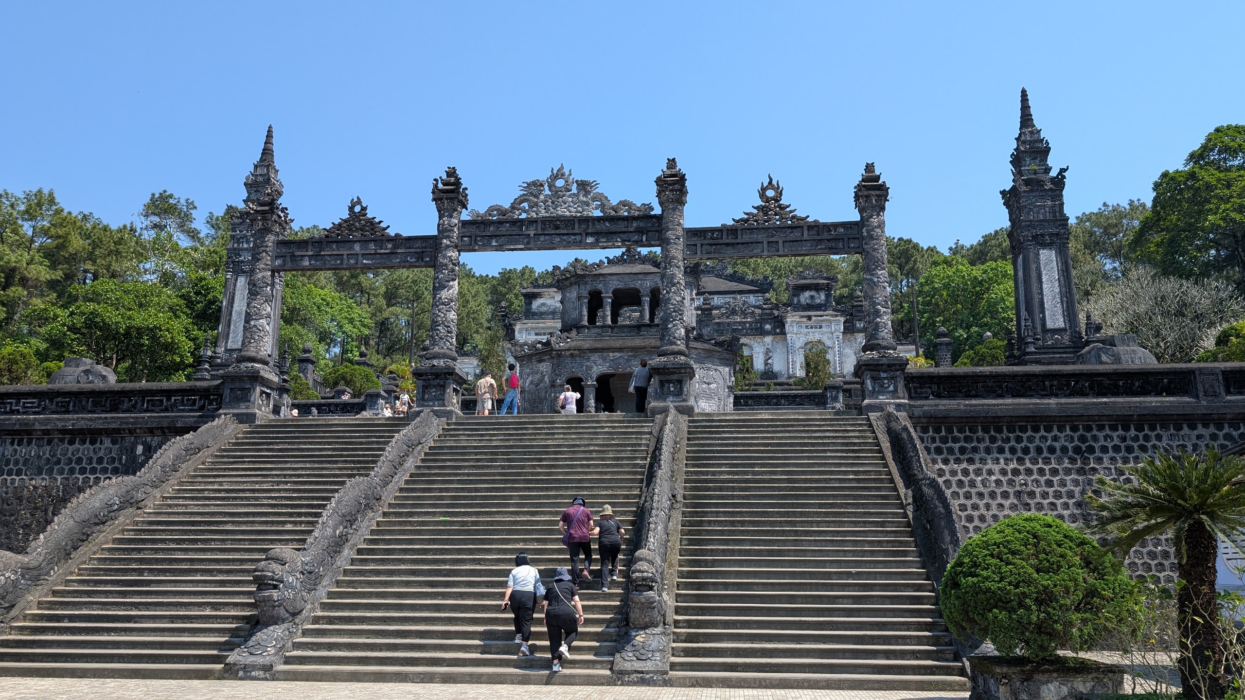 Wide stone staircase with carved dragon banisters leading up to the ornate gate of Khai Dinh's tomb in Hue