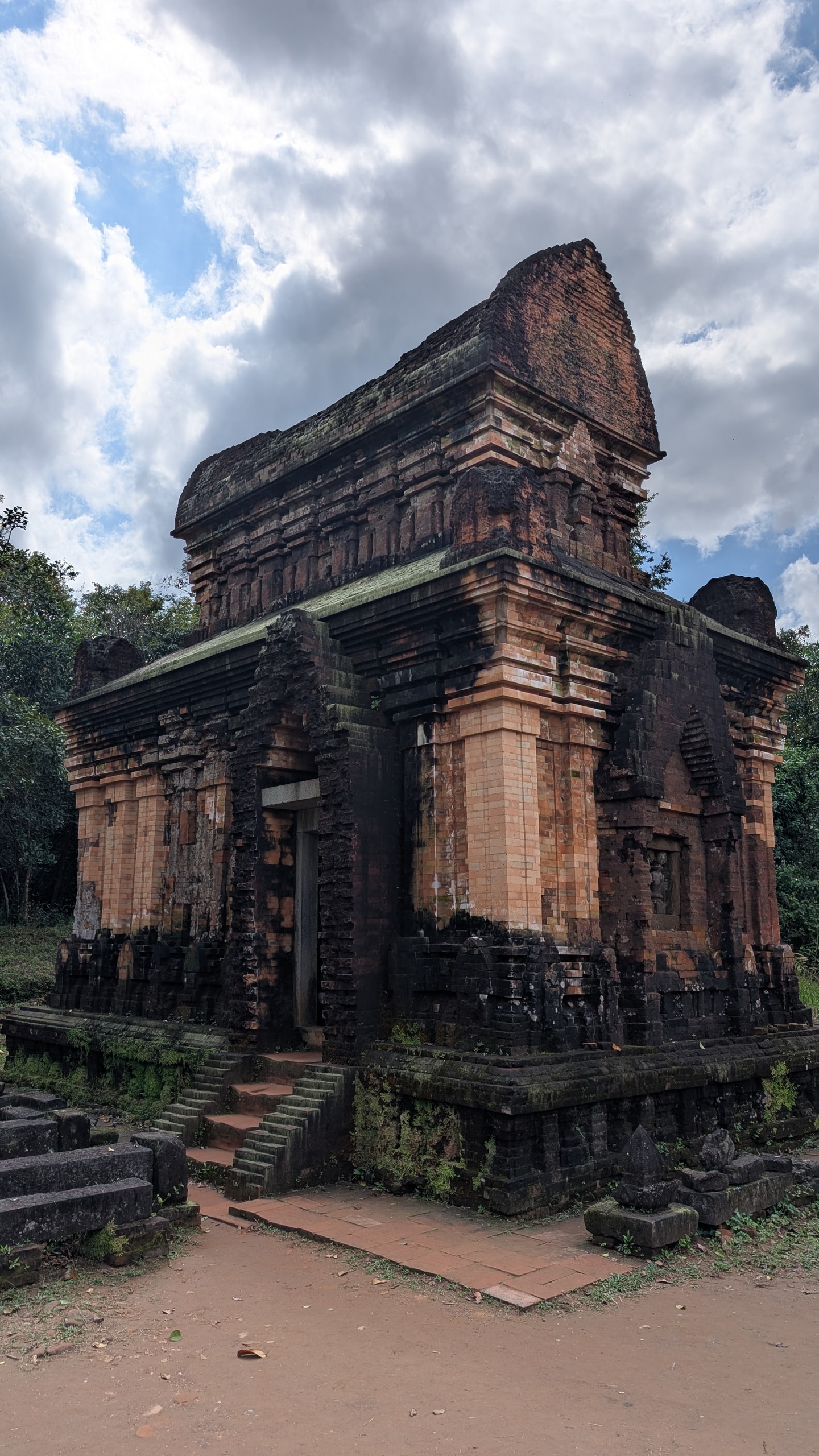 A tall red-brick Cham temple tower at Mỹ Sơn Sanctuary against jungle and a cloudy sky